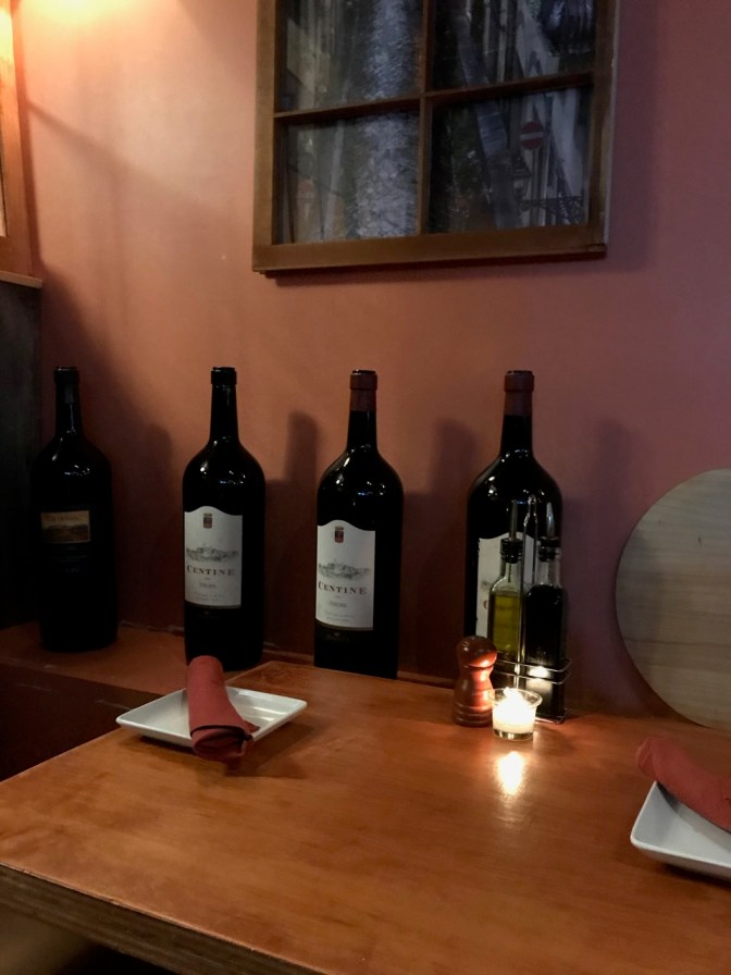 Table with candle on it, with wine bottles and fake window behind it.