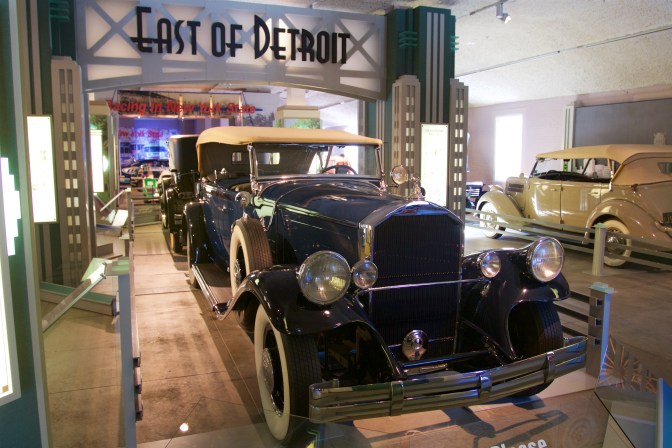 Blue Franklin touring sedan with art deco sign behind it saying EAST OF DETROIT.