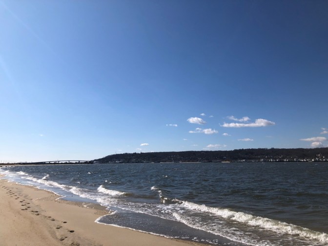 Coastline of Sandy Hook, with tree- and building-lined shore on opposite side.