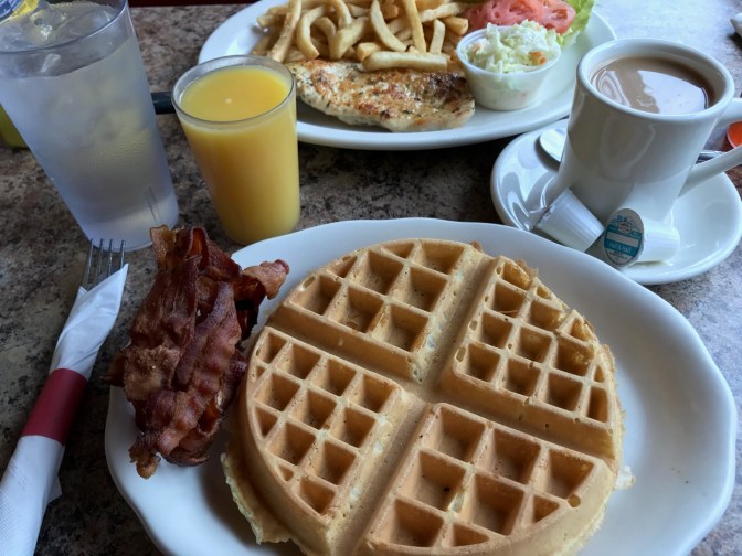 Waffle and bacon on white plate, with orange juice and coffee in cups.