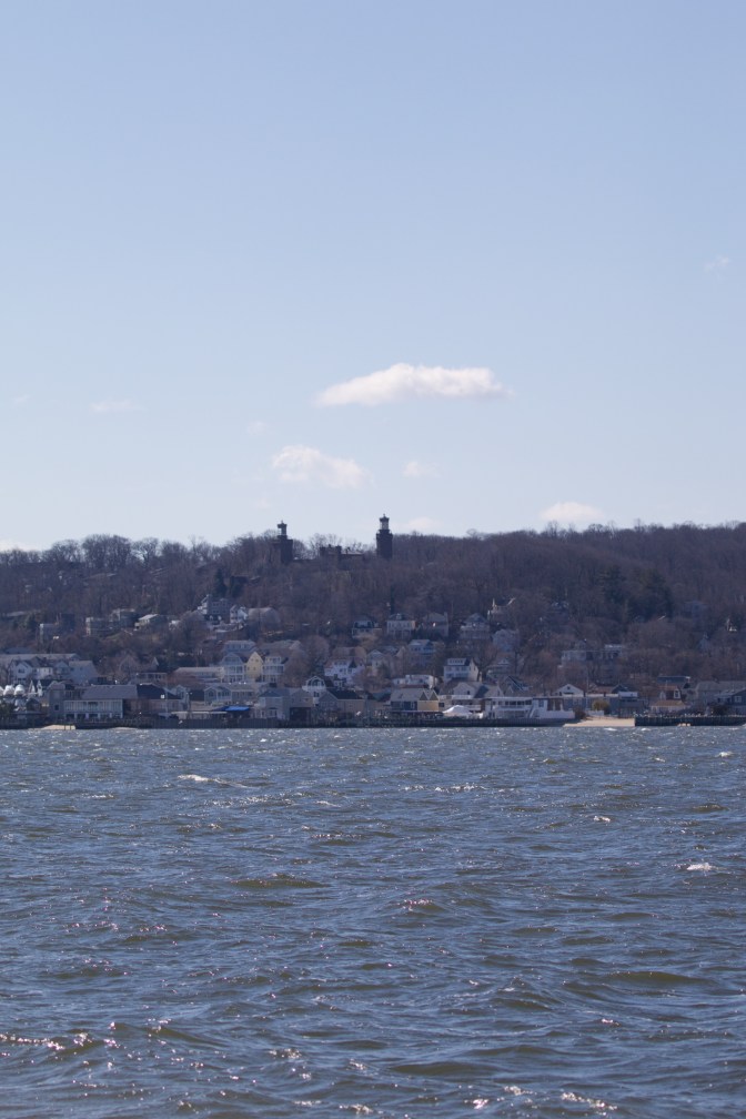 View of shoreline with houses long bottom of hill and Navesink Twins lighthouse at top.