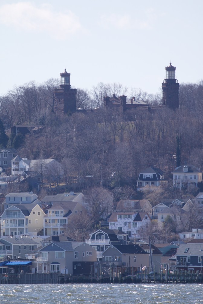 View of Navesink Twins lighthouse at top of hill, and buildings at bottom of hill.
