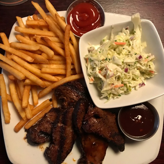 BBQ short ribs, french fries, and jicama slaw on a white plate, with BBQ sauce and ketchup in metal bowls.