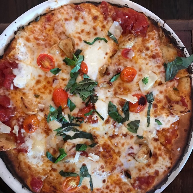Pizza topped with tomatoes, garlic, basil, and two different cheeses.
