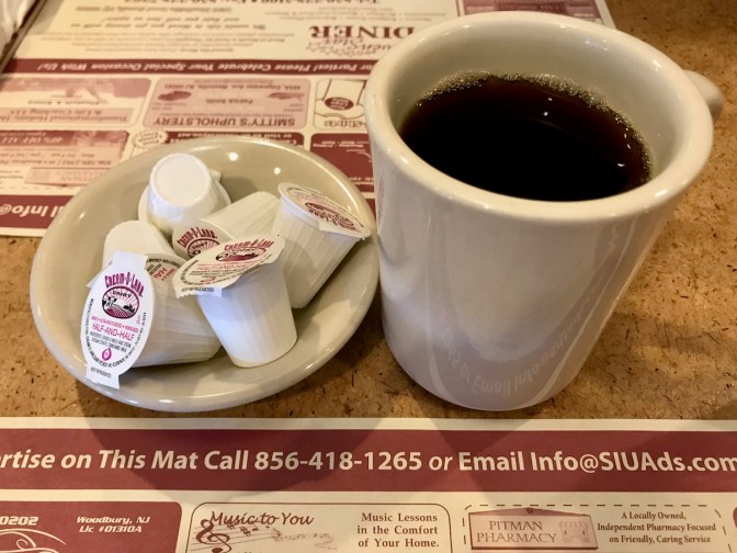 Cup of black coffee on table, with small dish of creamers beside it.