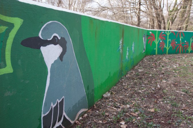 Mural of gray bird along green wall, with plants painted on wall in background.