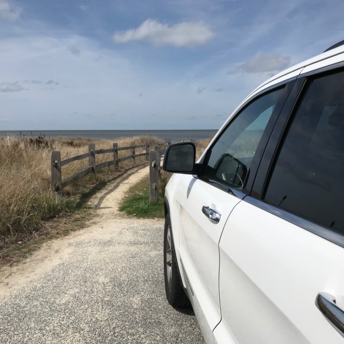 White 2014 Jeep Grand Cherokee parked in front of path leading to beach.
