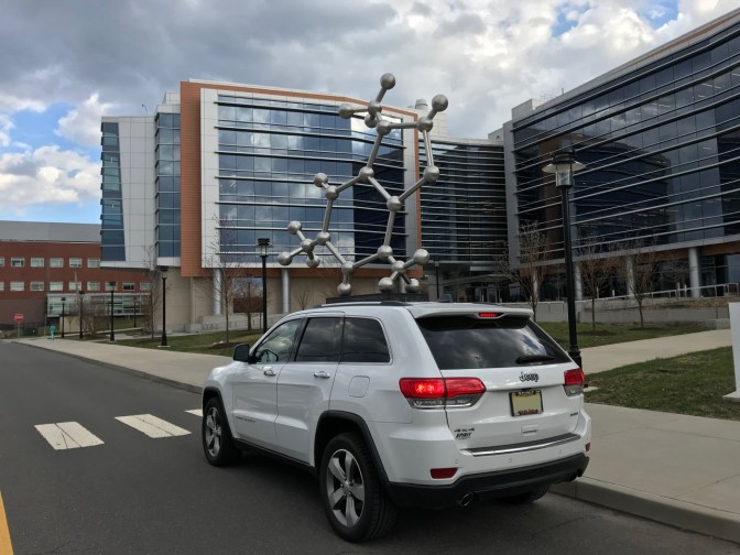 White Jeep Grand Cherokee in front of sculpture of caffeine molecule.