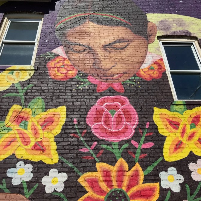 Mural of woman looking down upon four flowers, on side of brick building.