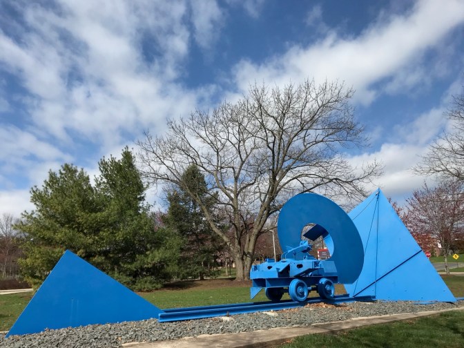 Blue train car on blue tracks, with geometric shapes on either end.