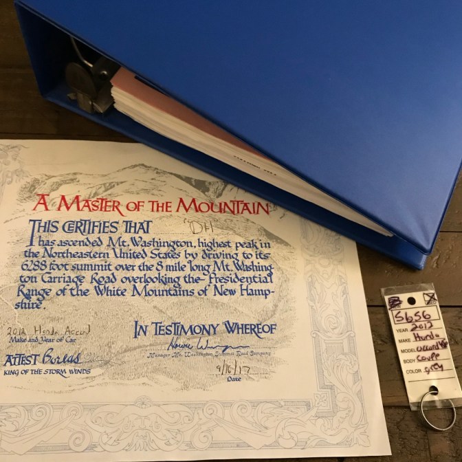Blue binder, keychain, and certificate of completion from Mt Washington, on wooden table.