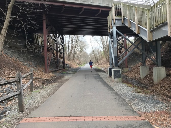 Greenway path running beneath a highway. A runner is ahead in the distance.