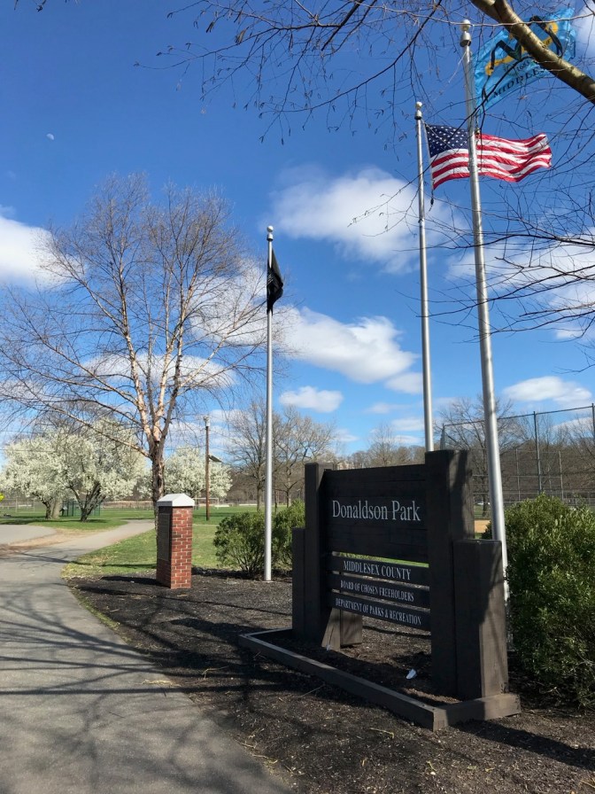 Park entrance with sign that says DONALDSON PARK. An American flag and a Middlesex County flag are flying above the sign.