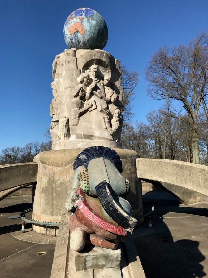 Section of fountain with sculpture of learning and scholars near globe at top of fountain.