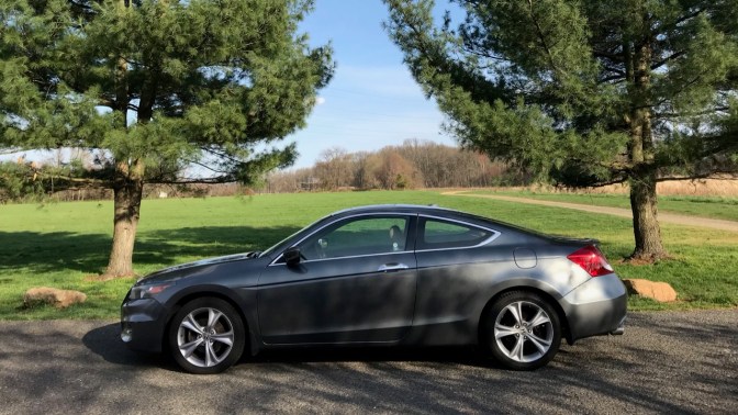 2012 Honda Accord coupe parked in front of trees, with an open field behind it.
