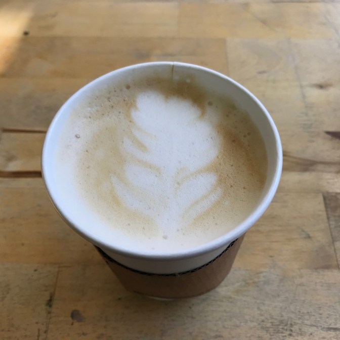 Close-up of cappuccino in paper cup with flower design in milk.
