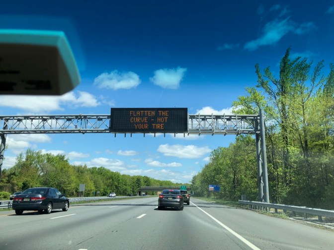 Sign over highway reading FLATTEN THE CURVE - NOT YOUR TIRE.