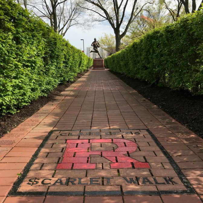 Shrub-lined brick Scarlet Walk, with statue of football player in background.