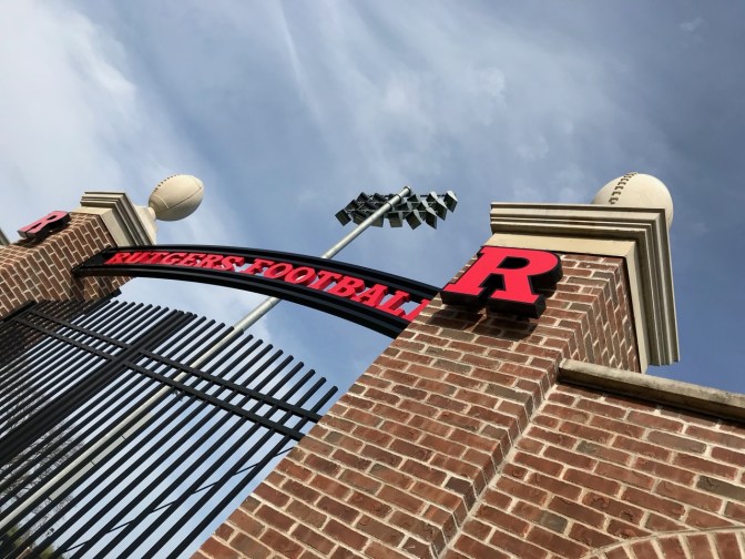Entrance to football practice fields, with brick gate and fence, and a sign that says RUTGERS FOOTBALL over gate.