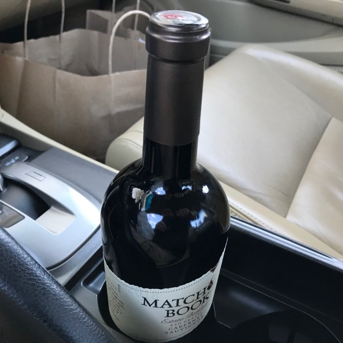Bottle of wine in center console of car, with bags of food.