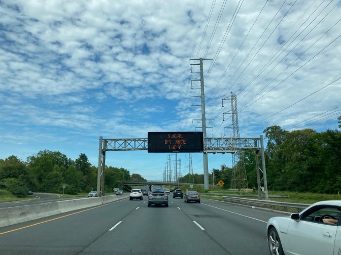 billboard over road that says SOCIAL DISTANCE TODAY.