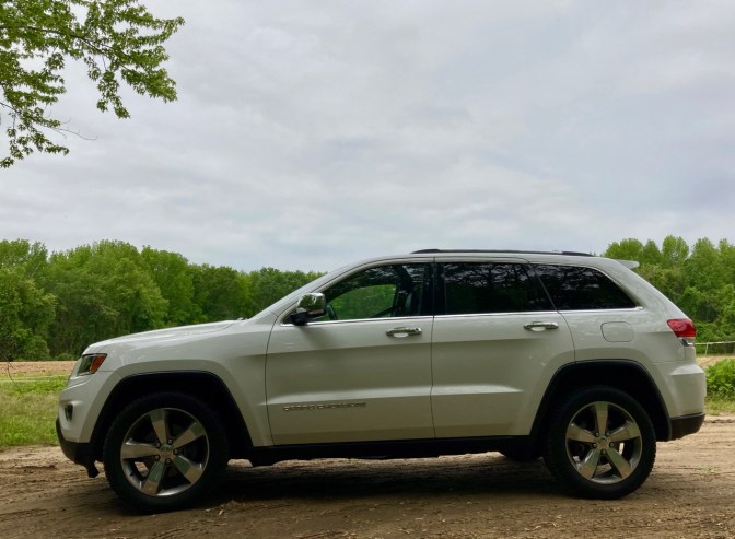 White Jeep Grand Cherokee parked on dirt trail, with treelike behind it.