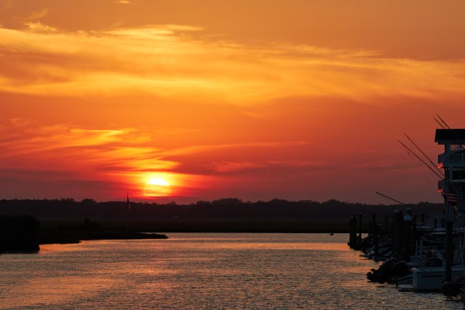 Sunset over bay, with houses along shore on right side of image.