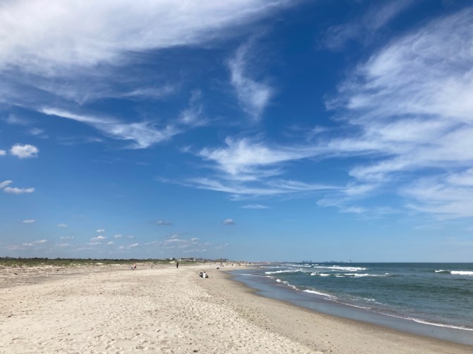 Nearly empty beach beside ocean, under a blue sky.