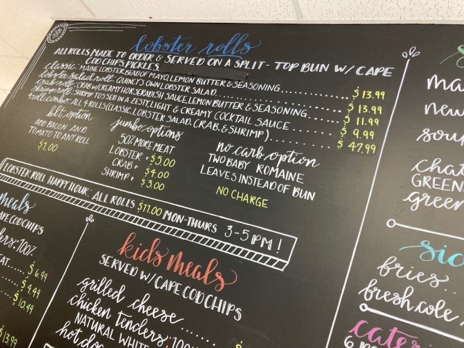 Chalkboard menu in restaurant listing lobster roll options.