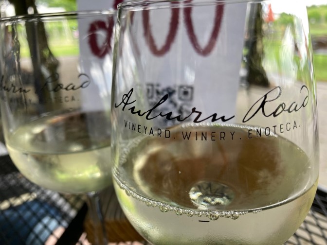 Two glasses of white wine on wrought iron table outside.