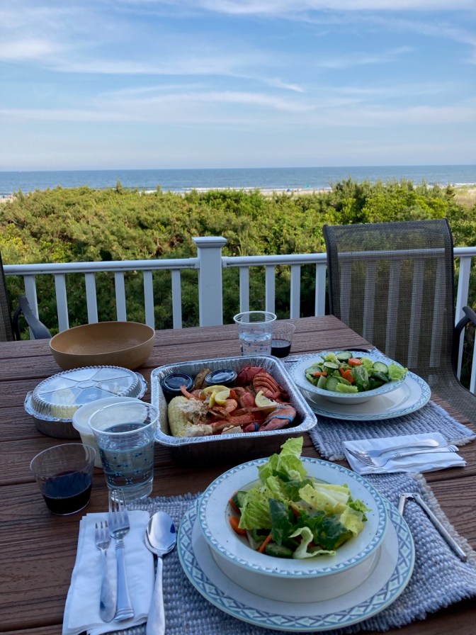 Porch table overlooking ocean, with salads and seafood platter on table.