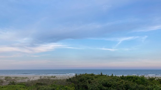 View of sky and ocean, with beach in foreground.