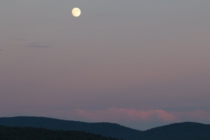 Full moon over mountains, with clouds low in the sky.