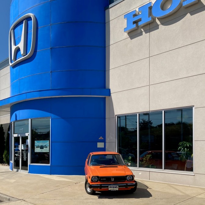 Exterior of Burns Honda, with a 1st generation orange Honda Civic parked in front of the building.