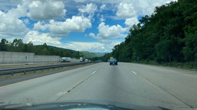 View of blue sky with clouds over NY Thruway, from behind windshield of Honda Accord.