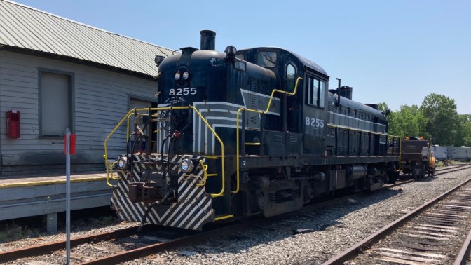Black railroad engine alongside maintenance depot.