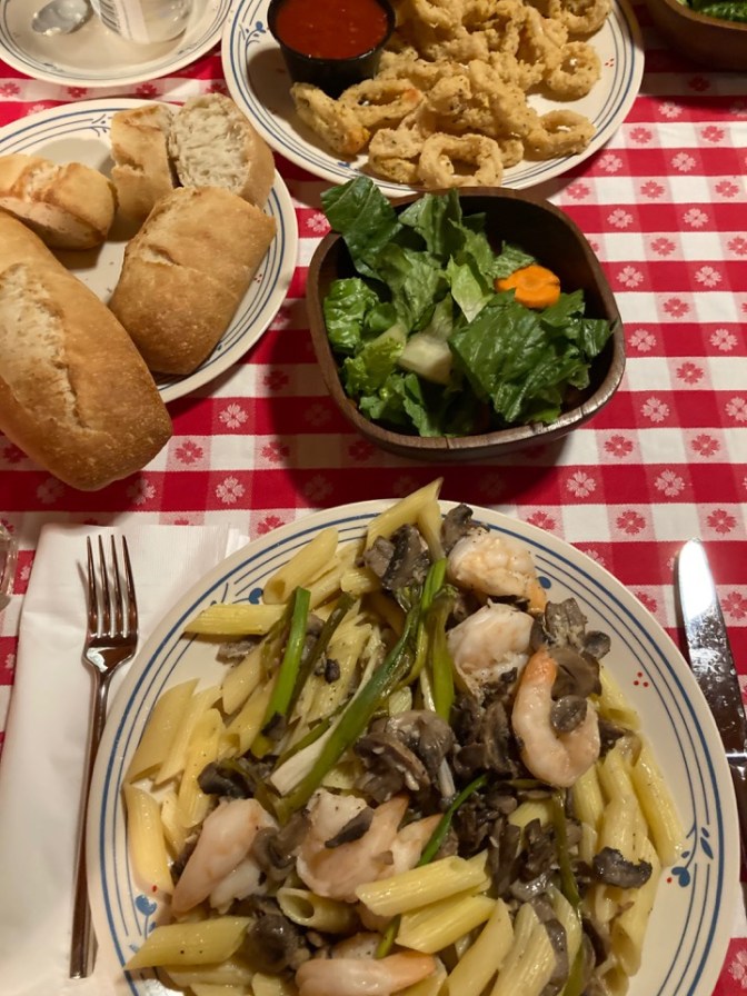 Table covered in red-and-white tablecloth, with plate of shrimp scampi, salad, fried calamari, and bread.