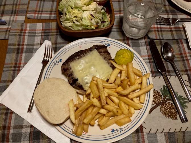 Cheeseburger and french fries on plate, with a salad in a bowl next to the plate.