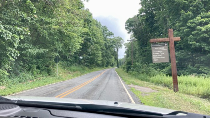 Tree-lined two-lane road with sign on right saying DELAWARE WATER GAP NATIONAL RECREATION AREA