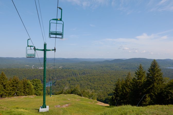 View of chair lift on mountain, with mountains and forests in distance.