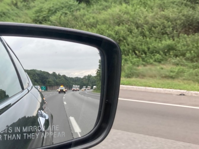 Rear view mirror of car with caravan of utility trucks.