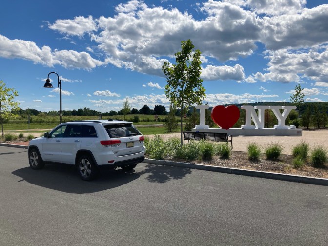 White Jeep Grand Cherokee parked in front of I HEART NY sign.
