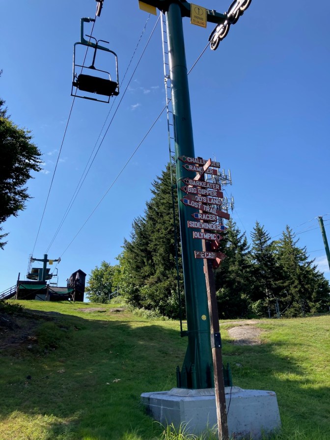 Chair lift, with sign in foreground indicating direction to different ski trails.