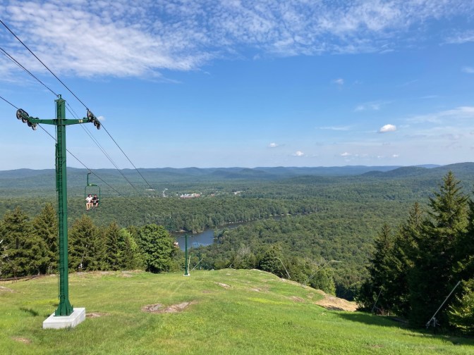 View of chair lift looking down the mountain, with two people riding in chair lift closest to camera.