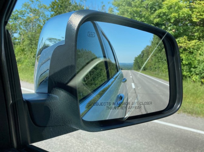 Car rearview mirror, with mountains in distance of mirror.