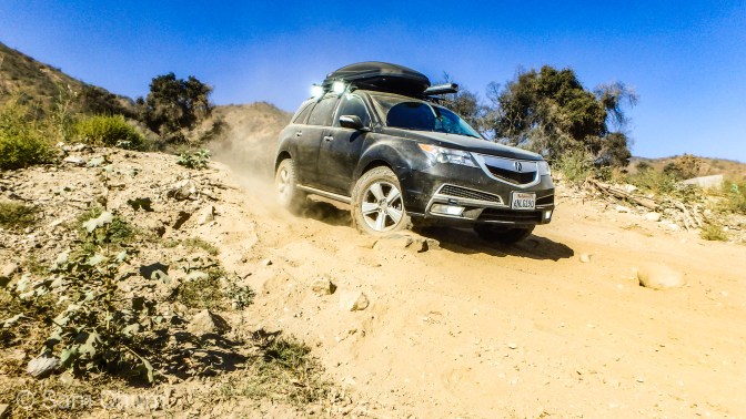 Black Acura MDX driving through sandy trail.