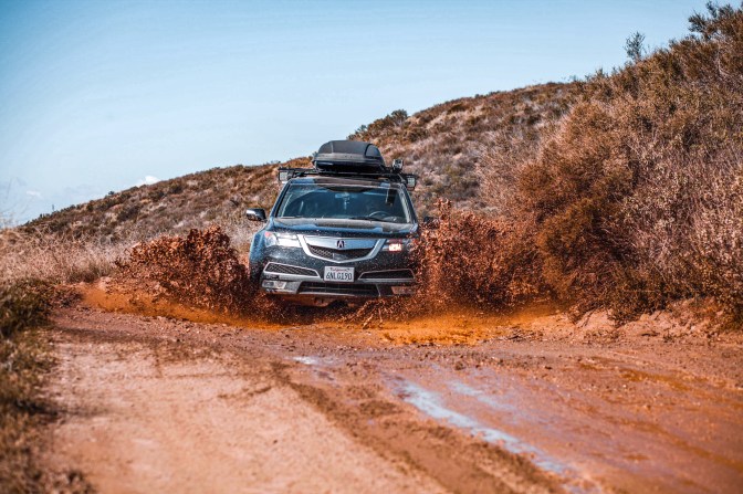 Black Acura MDX driving through a mud puddle.