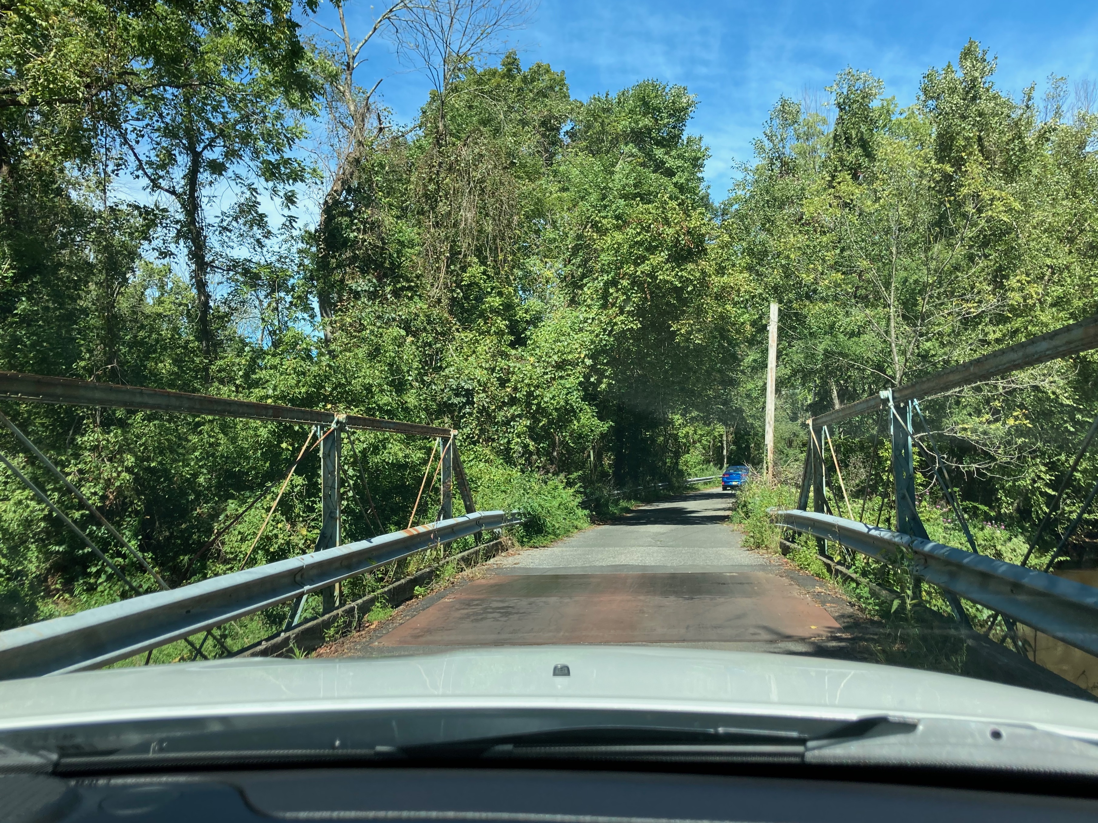 View of one-lane bridge, with the road continuing beyond into the woods.
