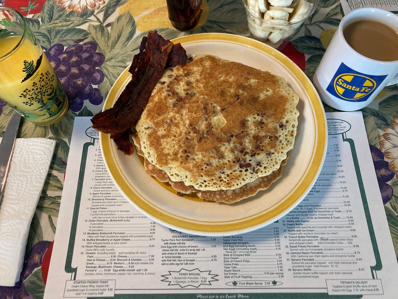 Plate with pancakes and bacon, glass of orange juice, and mug of coffee.