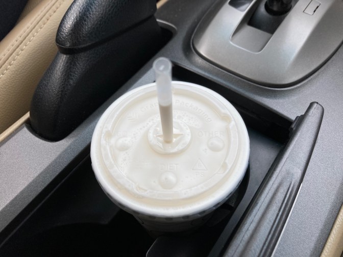 Vanilla milk shake in paper cup in cup holder of car.